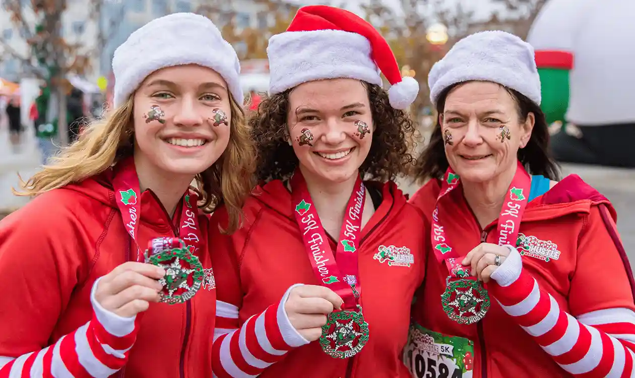 3 female Santa Hustle runners showing off their finisher medals